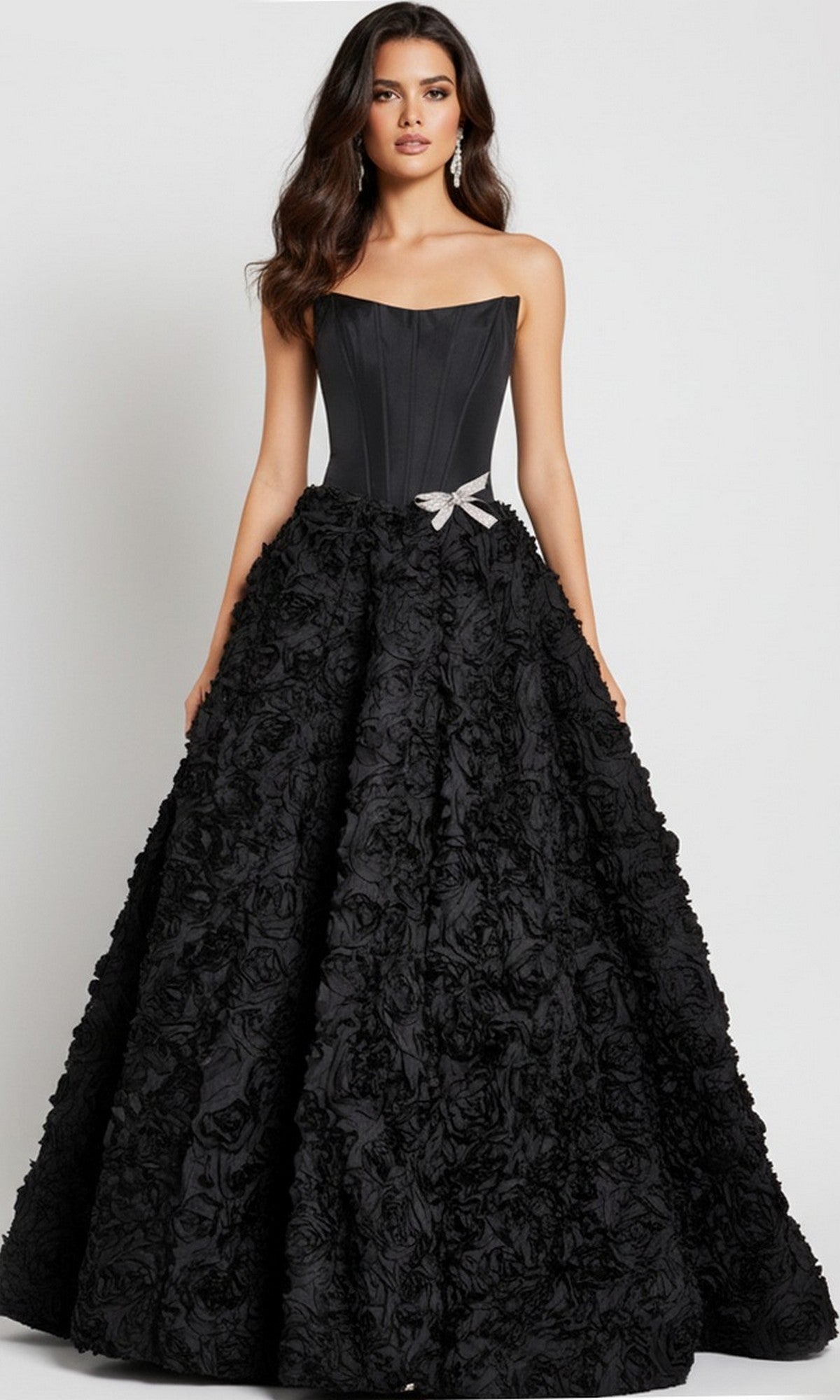A woman models the Jovani 47695 long prom dress, featuring a strapless corset bodice and textured 3D rosette skirt with a silver bow at the waist, posed against a plain background.